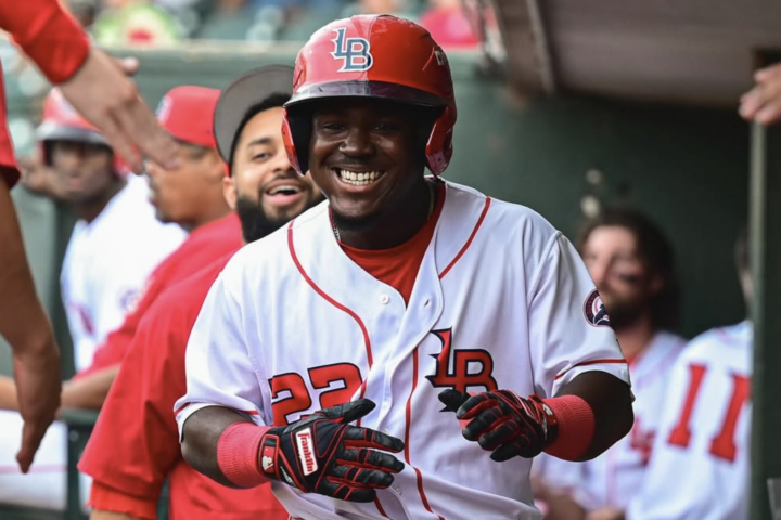 Baseball player in a white and red uniform smiles while walking through a dugout, surrounded by teammates giving high fives.